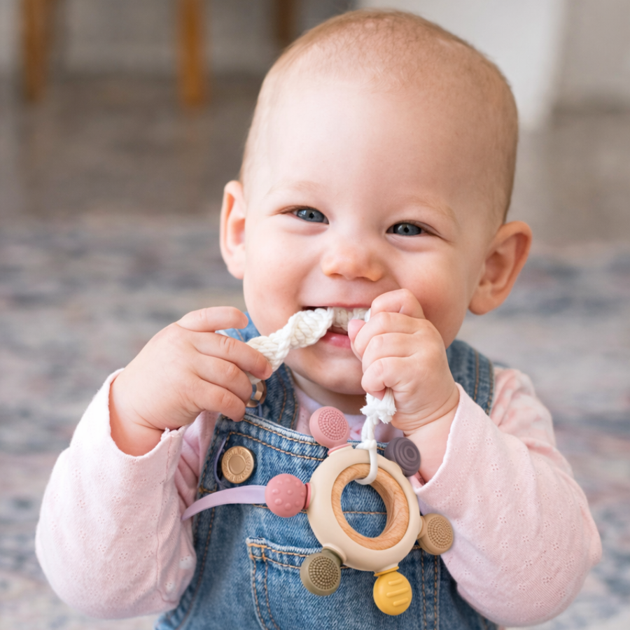Baby holding a silicone and wood teething ring in both hands.