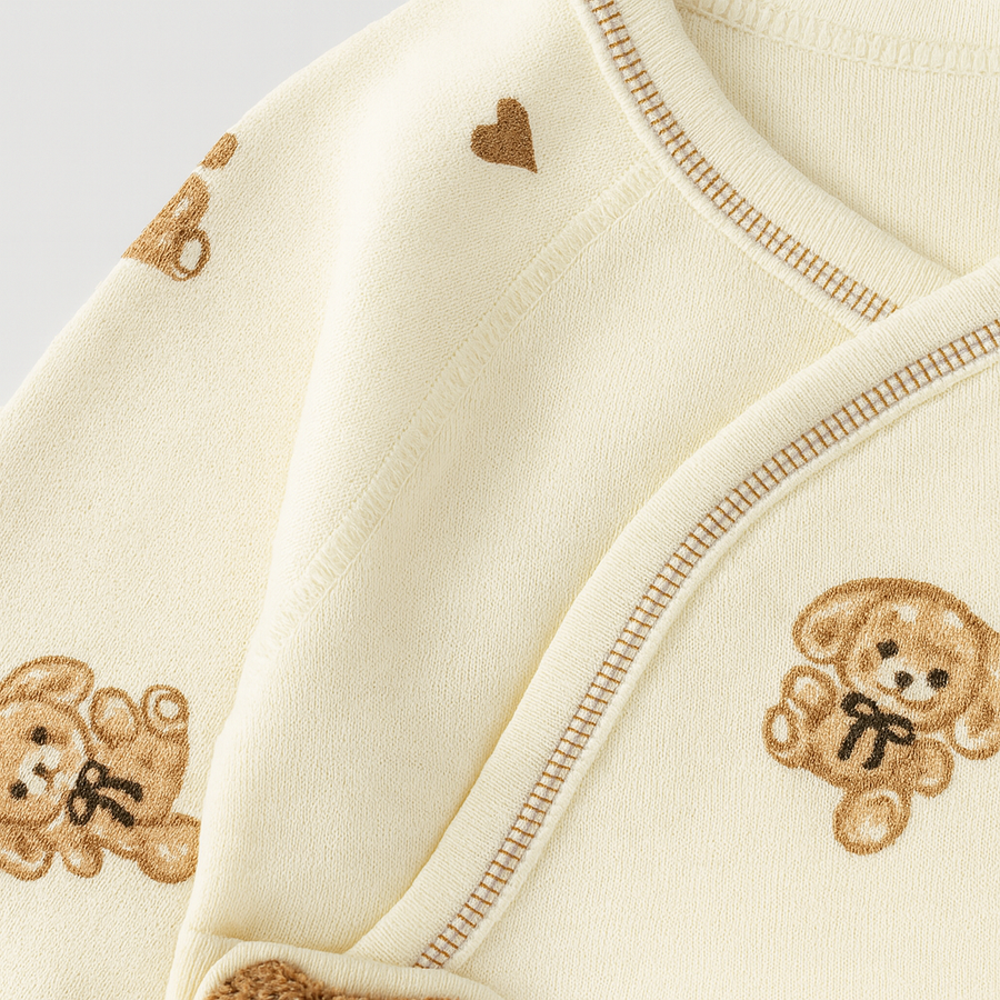 Front view of a cream baby footie sleepsuit laid flat with bear print detail