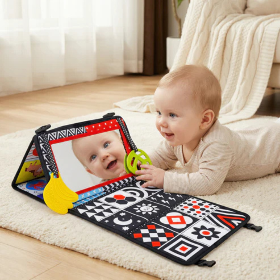 Baby lying on the floor playing with an open interactive mirror book.