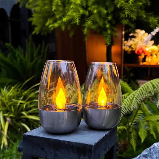 Stainless steel solar lantern glowing on a wooden table at dusk.