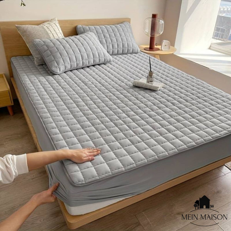 Quilted mattress cover shown in gray on a bed