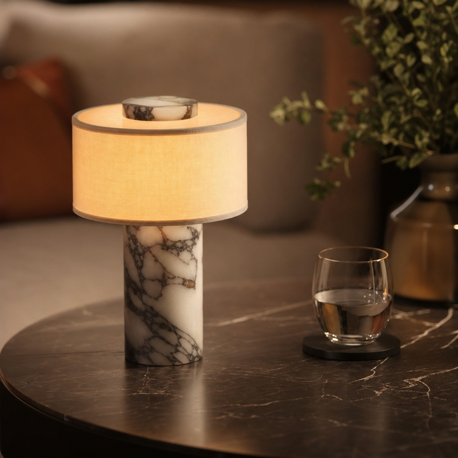 Marble and linen table lamp lit on a nightstand.