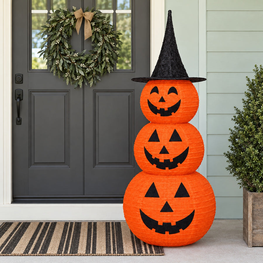 Stacked pumpkin decoration beside gray front door and wreath