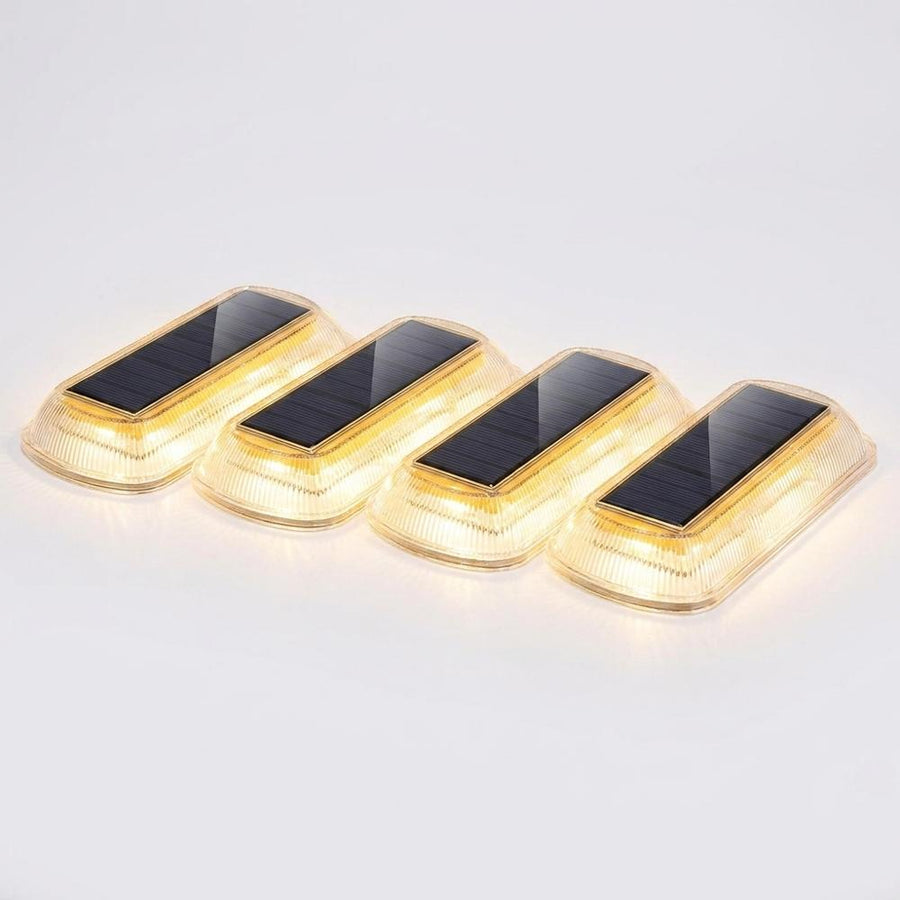 Four solar LED step lights on white background glowing warm white