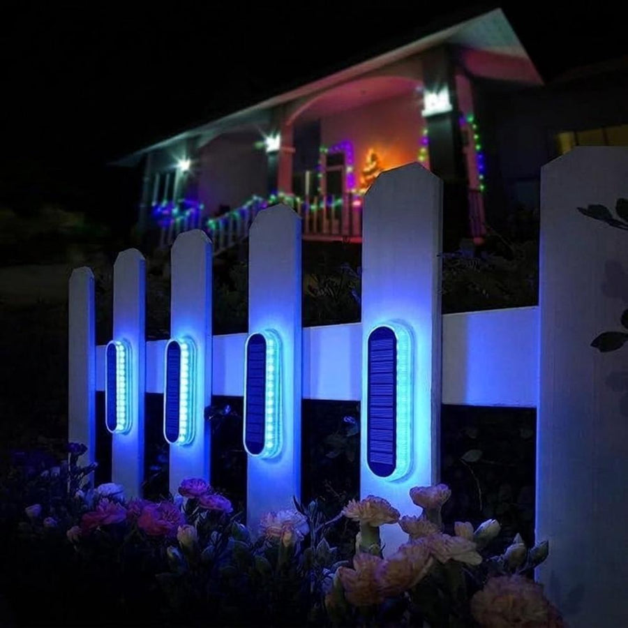 Blue solar fence lights glowing on white picket fence at night