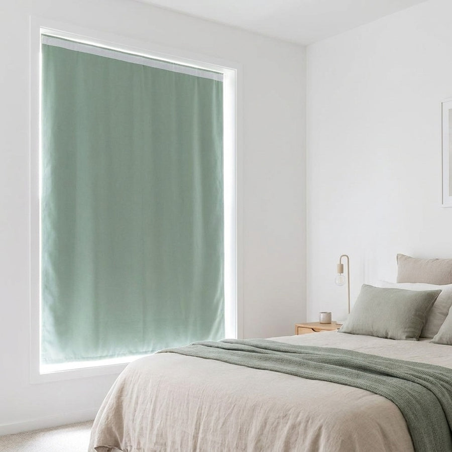 Light green blackout curtain installed on bedroom window, blocking sunlight