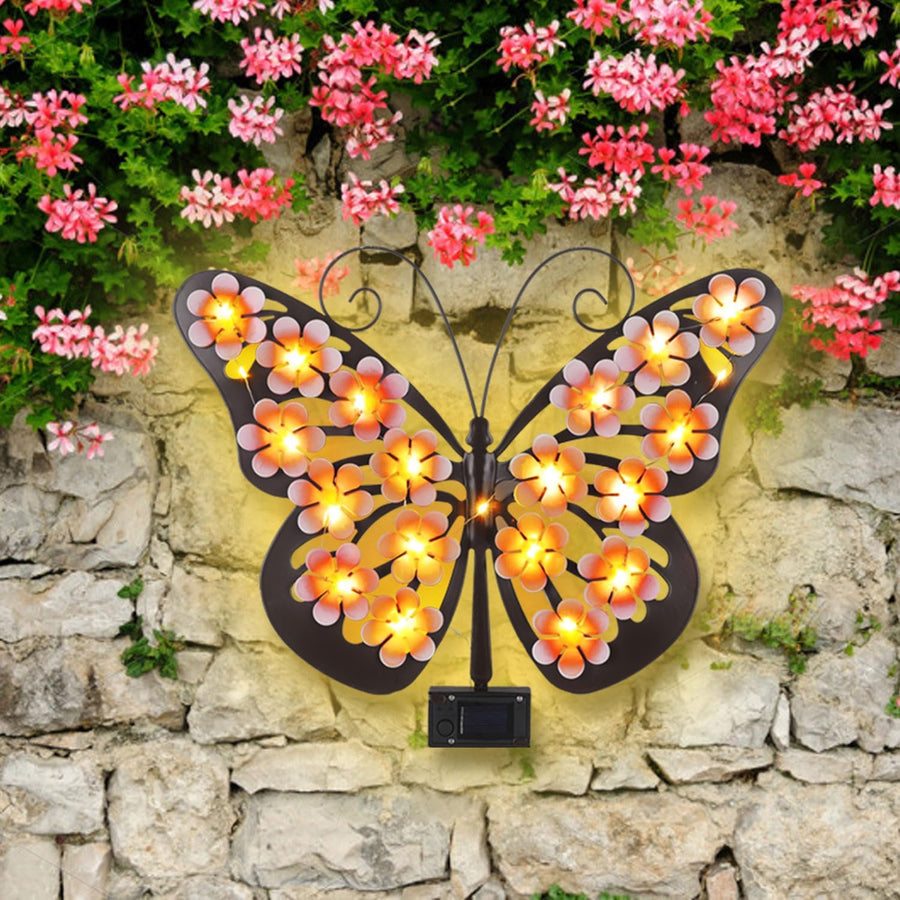 Solar butterfly on a stone wall with flowers – warm LED glow