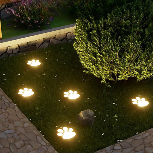 Solar-powered paw lights glow warmly on the lawn near a garden bed