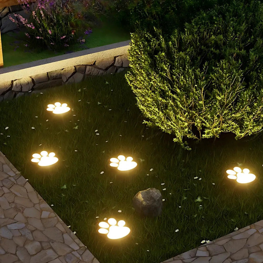 Solar-powered paw lights glow warmly on the lawn near a garden bed