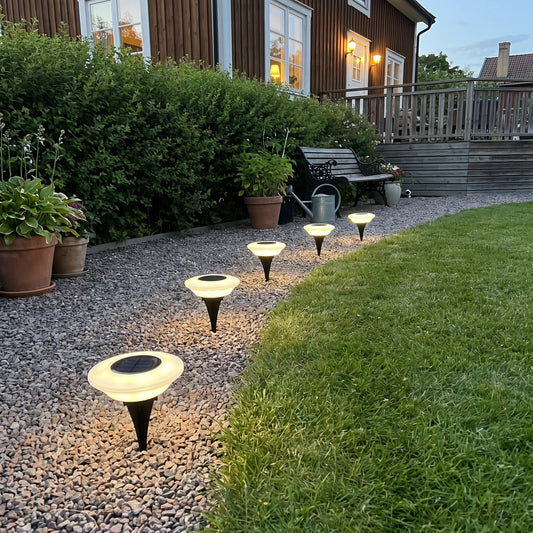 Warm white ground lights lining a gravel path on a summer evening
