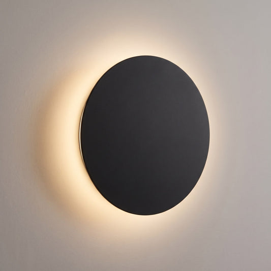 Black round LED wall light with a warm halo on the wall, eclipse design