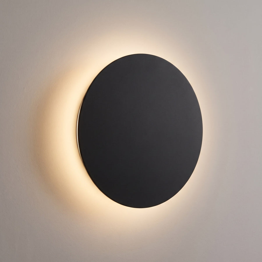 Black round LED wall light with a warm halo on the wall, eclipse design