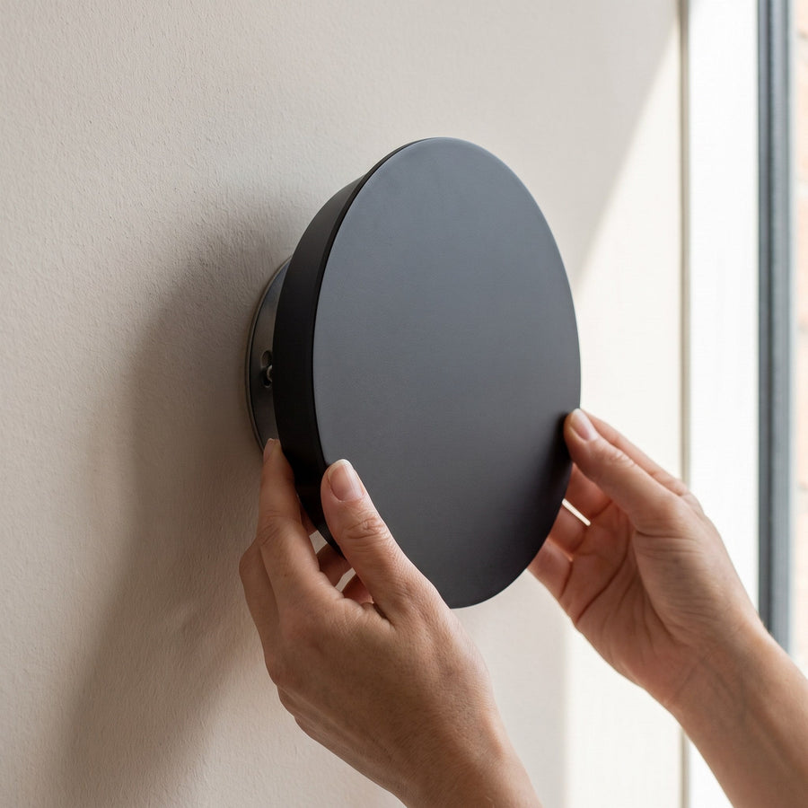 Hands mounting the round LED wall light onto the wall plate without tools